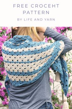 a woman wearing a blue and white crocheted shawl in front of pink flowers