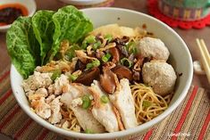 a bowl filled with noodles, meat and veggies next to chopsticks