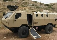 an armored vehicle parked on the side of a dirt road in front of a hill