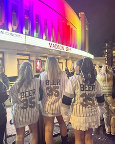 three girls dressed in baseball uniforms are walking down the street with their backs to each other