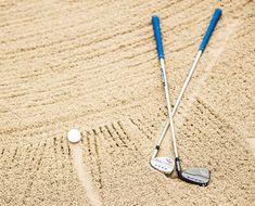 two golf clubs and a ball in the sand