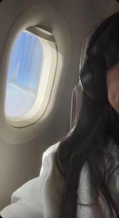 a woman wearing headphones looking out an airplane window