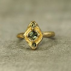 Description:  Born from the ocean, as though she was made long ago, dropped in the sea, then softened by years of dancing in the waves. The sapphires are a stunning, natural green that looks like seawater captured. It's low profile and soft textures make this ring so comfortable and perfect for daily wear.  Details:  -Solid 14k yellow gold  -Band is approx 2.5mm wide (top of the ring is approx 15mm x 11mm) -.5ct sapphire with adjacent 2.5mm round sapphires  -Size 5 1/4, but can be sized to your specifications. Contemporary Fine Jewelry, Round Sapphire, Jewelry Lookbook, Art Deco Earrings, Silver Work, Put A Ring On It, Dream Jewelry, Jewelry Inspo, Low Profile