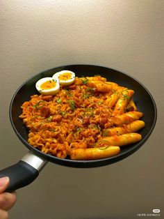 someone is holding a frying pan full of pasta and eggs