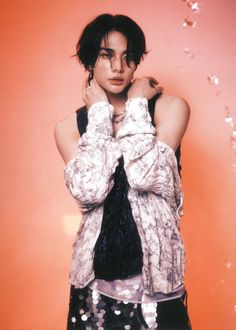 a woman with her hands on her face standing in front of an orange wall wearing a black and white scarf