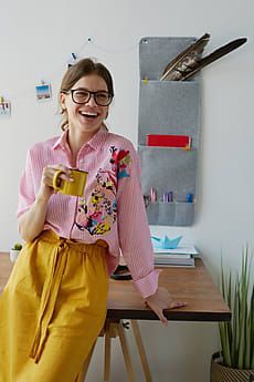 a woman sitting at a desk with a cup in her hand, smiling and holding a coffee mug