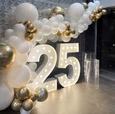 the number twenty five surrounded by white and gold balloons