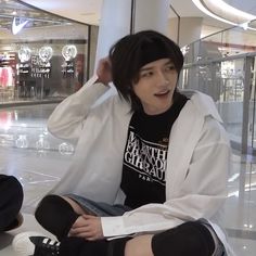 a young man sitting on the ground with his hands in his hair and wearing a white jacket