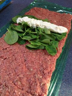 raw ground beef with spinach leaves and feta cheese on the top, ready to be cooked