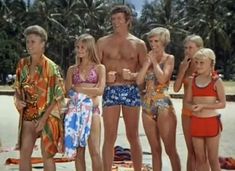 a group of young people standing on top of a beach next to the ocean and palm trees