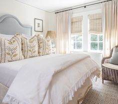 a bed with white linens and pillows in a bedroom next to a wicker chair