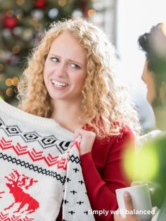 a woman holding up a sweater in front of a christmas tree