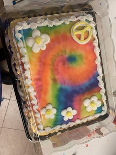 a tie dye cake sitting on top of a plastic container filled with icing and flowers