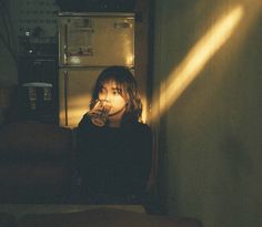 a woman sitting in front of a refrigerator with light coming through the door and on her face