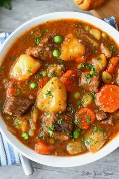 a bowl of hearty beef stew with carrots, potatoes and parsley on the side