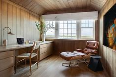 a room with wood paneling and a chair in front of a window that has a painting on the wall