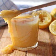 a glass filled with liquid sitting on top of a wooden table next to sliced lemons