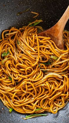 a wok filled with noodles and vegetables being stirred by a wooden spoon in it