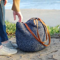 a person standing on the beach with a handbag in front of them and grass