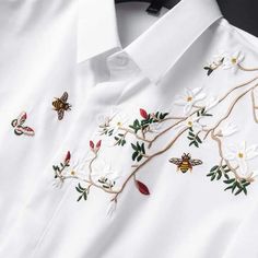 a white shirt with embroidered flowers and bees on the chest, sitting on a black surface