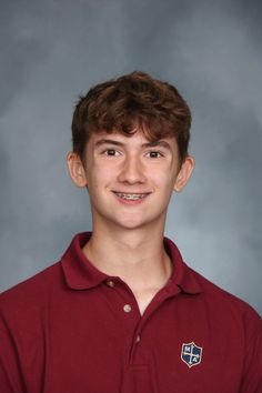 a young man wearing a maroon shirt and smiling at the camera in front of a gray background