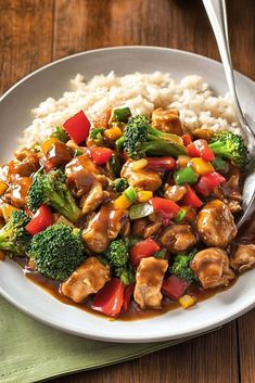 a white plate topped with chicken and veggies next to rice on top of a wooden table