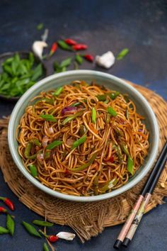 a bowl filled with noodles and vegetables next to chopsticks on a table top