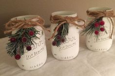 three mason jars with pine branches and berries tied to the lids are sitting on a bed