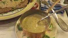 a bowl of soup is sitting on a plate next to some meat and gravy