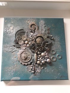 an art piece is hanging on the wall in front of a white frame with blue and silver designs