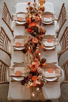 the table is set with white linens and orange flowers, candles and place settings