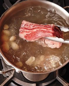 the meat is being cooked in the pot on the stove with a ladle full of water