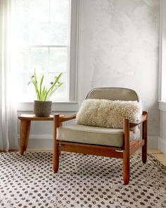 a living room with a chair, table and potted plant in the window sill