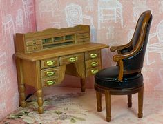 a doll house desk and chair in front of a pink wall with drawings on it