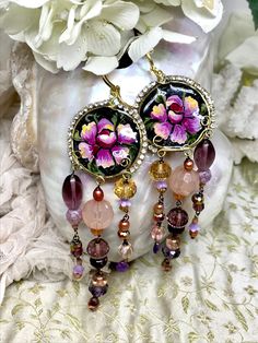 "DUSTY ROSE TRAILS  A beautiful and dramatic handmade pair of OOAK  earrings, featuring a cameo embellished with hand painted flowers, and edged with vintage rhinestones. The cameo is made from hand shaped and hammered brass wire, filled with resin. Trails of vintage glass beads, freshwater pearls and Amethyst briolettes dangle below the cameos.      * Lightweight     * Resin     * Entirely hand modelled, no moulds used.     * Leverback earwires     * Amethyst briolettes     * Czech glass beads Bohemian Jeweled Chandelier Earrings As Gift, Bohemian Jeweled Beaded Dangle Earrings, Bohemian Style Jeweled Beaded Dangle Earrings, Bohemian Jeweled Dangle Beaded Earrings, Bohemian Jeweled Beaded Earrings For Gifts, Bohemian Jeweled Purple Jewelry, Hammered Brass, Hand Model, Hand Painted Flowers