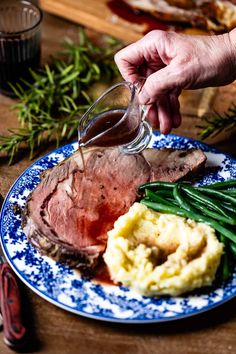 a plate with meat, mashed potatoes and green beans is being drizzled