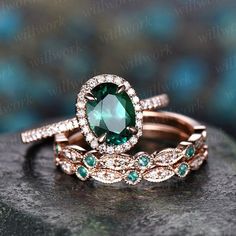 two wedding rings with green and white stones on top of each other, sitting on a rock