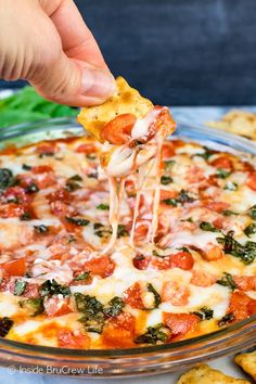 a hand holding a piece of pizza with cheese and spinach on it, being lifted from a casserole dish