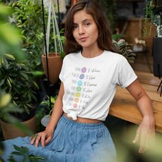 a woman sitting on a bench in front of potted plants wearing a white t - shirt