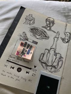 an open book with drawings on it next to a cell phone and some other items