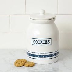 a cookie jar sitting on top of a white counter next to two oatmeal cookies