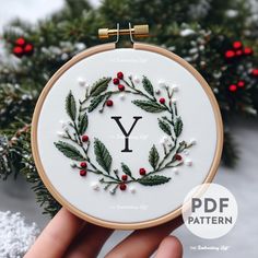 a hand embroidered wreath with the letter y on it is shown in front of snow and evergreen branches