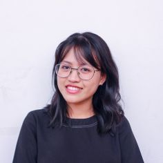 a woman wearing glasses standing in front of a white wall with her arms crossed and smiling at the camera