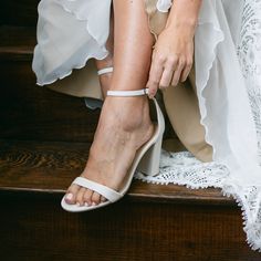 a woman wearing white shoes sitting on top of a set of stairs with her legs crossed