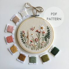 a cross stitch pattern with flowers and leaves on it, surrounded by spools of thread