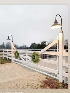 a white fence with wreaths on it and two lights hanging from the top one