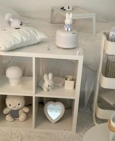 a white shelf with stuffed animals on top of it next to a bed and pillows