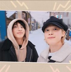 two people standing next to each other in front of snow covered street with buildings behind them