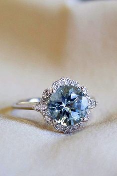 an engagement ring with a blue topaz surrounded by diamonds on a white cloth background