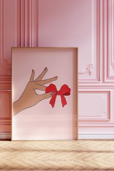 a hand holding a red bow in front of a pink wall